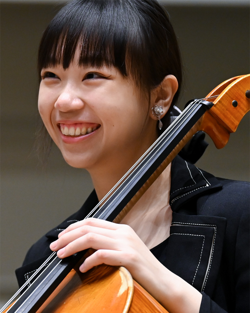 A female student, wearing smart black attire, holding a cello, smiling at the camera.